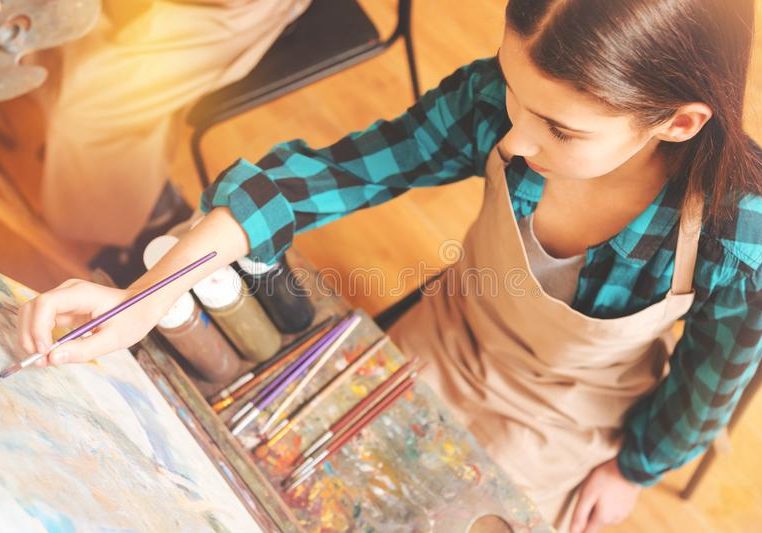 teenage-girl-focusing-art-canvas-painting-magical-process-top-view-young-lady-wearing-apron-holding-brush-100580514